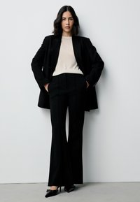 Black tailored blazer over a beige ribbed sweater, paired with black flared trousers and black pointed-toe heels. Smooth and structured fabrics.