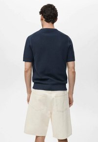 Maglione a maniche corte in maglia di color navy con un motivo testurizzato, abbinato a pantaloni corti leggeri a lunghezza ginocchio con tasche posteriori.