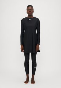 Juodas ilgomis rankovėmis tunikos suknelė su apvaliu iškirpimu, derinama su juodomis legging'ais. Pabrėžia baltus „Nike“ logotipo akcentus ant krūtinės ir kojų.
