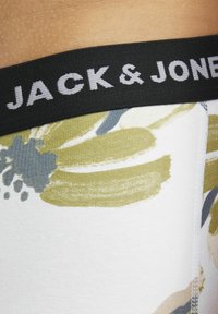 Weiße Unterwäsche mit grünen und blauen abstrakten Pinselstrichmustern, ausgestattet mit einem schwarzen Gummibund, auf dem "JACK & JONES" in Grau gedruckt ist.