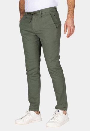 Olijfgroene taps toelopende broek van een textuurstof, met zijzakken en een trekkoord in de taille, gecombineerd met witte sneakers.