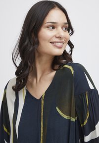 Blusa blu navy larga con scollatura a V, caratterizzata da vivaci motivi astratti in giallo e crema, con maniche a palloncino texturizzate.
