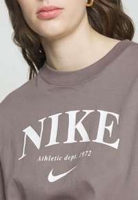 Felpa in cotone marrone con un grande logo bianco "NIKE" e la scritta "Athletic dept. 1972", con collo rotondo e texture morbida.