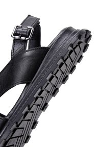 Sandal nero con tomaia in materiale sintetico e cinturino regolabile con fibbia. La suola in gomma testurizzata presenta un battistrada profondo per aderenza e durata.