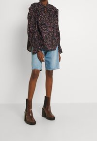 Svart blommig blus med puffärmar, volangkrage och nyckelhålsdetalj, tillsammans med ljusblå denimshorts och glänsande bruna klackstövlar.