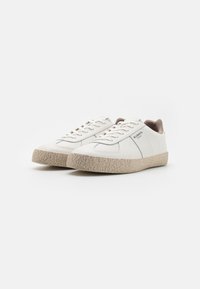 Hvide lædersneakers med en struktureret beige sål, der har et enkelt design, flade snørebånd og diskret branding på siden.