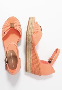 Korálové klínové sandály s pletenou jute platformou, otevřená špička s textilním mašlí, nastavitelný pásek na kotníku a branding Tommy Hilfiger uvnitř.