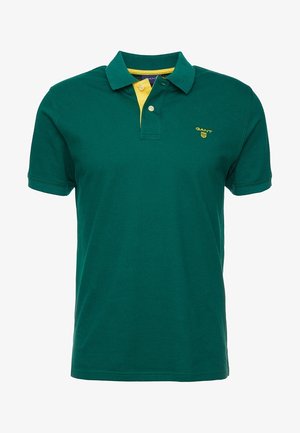 Polo de manga corta en verde oscuro con tapeta interna amarilla y pequeño logo GANT amarillo en el pecho izquierdo.