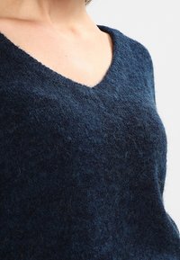 Donkerblauwe wollen gebreide trui met een V-halsontwerp, met een zachte, gestructureerde oppervlakte en een iets losse pasvorm. Geen zichtbare patronen of accenten.