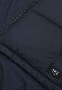 Navy puffer jacket with a vertical zipper, quilted texture, and a woven VANS label. Smooth finish and lightweight design.