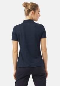 Donkerblauwe polo met een kraag, korte mouwen en een aansluitend ontwerp. Glad textuur met een subtiel patroon, zichtbare stiksels en geen logo's.