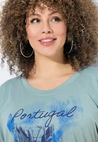 Camiseta de color azul claro con cuello redondo, con gráficos azules y la palabra "Portugal". Material de algodón suave, ajuste relajado y mangas cortas.