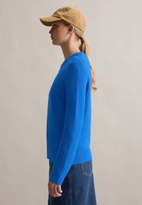 Niebieski dziergany sweter z długimi rękawami, okrągłym dekoltem i prążkowaną fakturą, zestawiony z beżową czapką z daszkiem i spódnicą dżinsową.