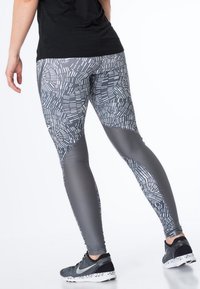 Sportovní legíny s šedým abstraktním vzorem, texturovanými panely a přiléhavým střihem. Materiál je elastický a prodyšný, vhodný pro cvičení.