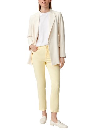Blazer crema, t-shirt bianca e pantaloni giallo pallido, abbinati a mocassini chiari; texture morbide e vestibilità su misura in tutto l'insieme.