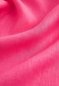 Tissu rose vif avec une texture tissée visible, plié doucement pour créer des courbes et des ombres douces.