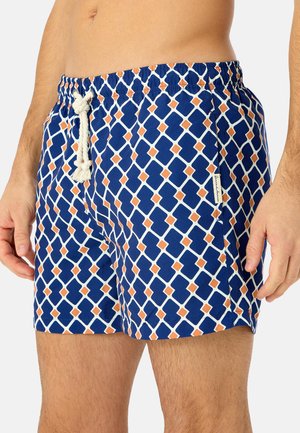 Mann trägt blaue Badeshorts mit weißem und orangefarbenem geometrischem Diamantmuster und einer weißen Kordel am Bund.