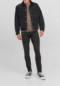 Svart denimjacka med två framfickor, ihop med en grå t-shirt och svarta tajta jeans. Bärs med svarta och vita sneakers.