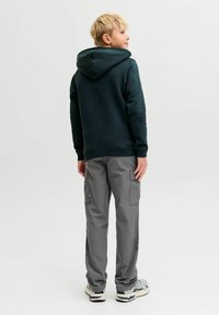 Tamnozeleni dukserica s kangaroo džepom sprijeda, u kombinaciji s svijetlim sivim cargo hlačama. Teksturna tkanina i dizajn s kapuljačom.