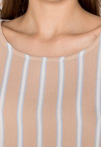 Ljusbeige topp med horisontella blå ränder. Mjukt, lätt tyg och rundad halsringning. Synliga sömmar längs kragen.