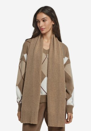 Sciarpa beige lavorata a maglia con una texture morbida, caratterizzata da un bordo a coste, mostrata insieme a un maglione con motivo in toni caldi di marrone e crema.