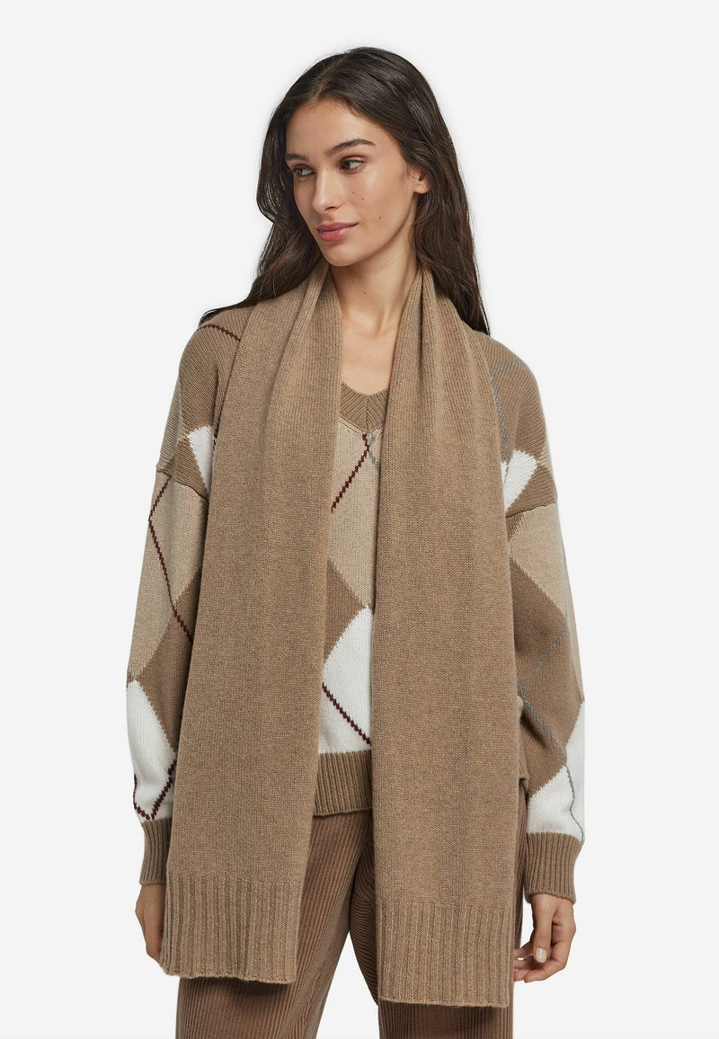 Beżowy, dziergany szalik o miękkiej fakturze, z prążkowanym brzegiem, prezentowany razem z wzorzystym swetrem w ciepłych odcieniach brązu i kremu.