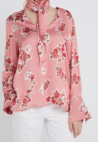 Blusa floreale rosa in satin, con scollatura a V, maniche lunghe con polsini svasati e una sciarpa abbinata legata al collo.