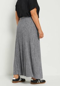 Jupe maxi plissée grise en tissu texturé ; associée à des baskets noires avec des rayures blanches et une semelle en caoutchouc. Vue de dos affichée.