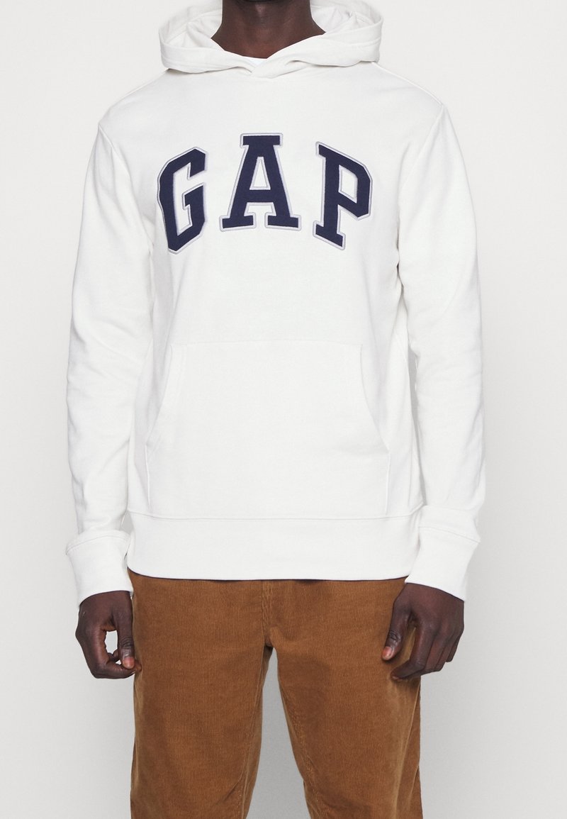 Felpa bianca con grande logo "GAP" in blu navy sul petto, tasca a marsupio e cappuccio regolabile. Tessuto in cotone morbido con polsini a costine.