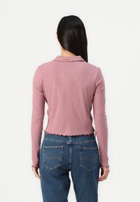 Ribbet langermet topp i mauve, med krage og bølget kant, sammen med høywaisted blå denimjeans.