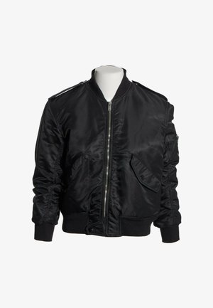 Chaqueta bomber negra de satén con cremallera frontal, puños y cinturilla acanalados, bolsillos con solapa y hombreras en un torso de maniquí blanco.
