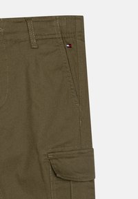 Pantaloni cargo verde oliva con tasca a toppa, passanti per cintura e cuciture a contrasto. Presenta un piccolo etichetta con logo con accenti rosso, bianco e blu.