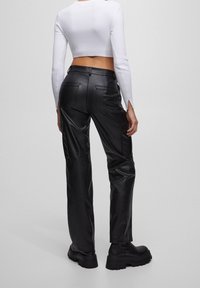 Pantalon cargo en cuir noir avec une silhouette ajustée, doté de poches latérales, de poches arrière, et d'une texture lisse. Complété par des bottes noires épaisses.