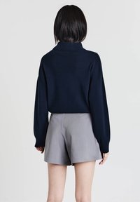 Maglione lavorato a maglia blu navy con colletto alto e vestibilità comoda, abbinato a pantaloni corti grigi chiari su misura. Texture liscia, maniche lunghe e senza motivi visibili.