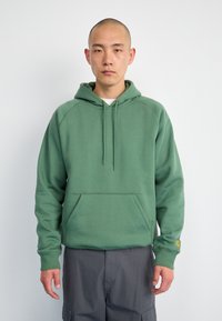 Sudadera verde con un bolsillo estilo canguro, cordones ajustables, puños acanalados y un corte relajado. Tejido suave con un acabado texturizado.
