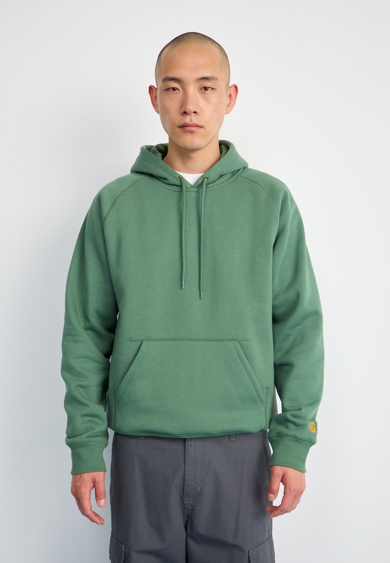 Sudadera verde con un bolsillo estilo canguro, cordones ajustables, puños acanalados y un corte relajado. Tejido suave con un acabado texturizado.