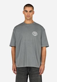 Pelēks īsām piedurknēm t-krekls, izgatavots no kokvilnas, ar apaļu kaklu un nelielu drukātu dizainu kreisajā krūšu daļā. Gadījuma piegriezums.