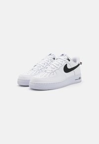 Baltie Nike Air Force 1 kedas ar melnu swoosh, perforētu purngali, plakaniem šņorēm un teksturētu gumijas zoli. Izcelts ar zīmola logo uz mēles.