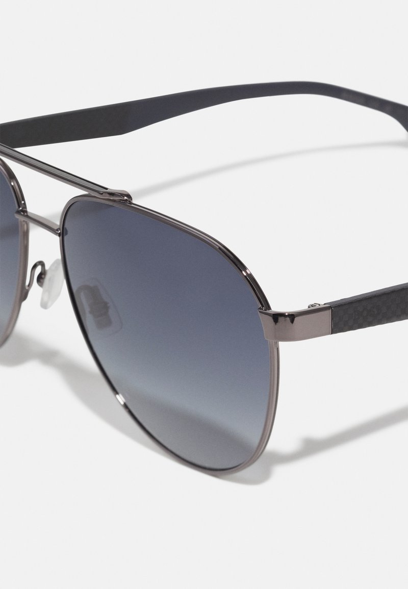 Lunettes de soleil avec une monture en métal bicolore, des verres dégradés foncés et des branches en plastique noir texturé. Équipées de plaquettes de nez ajustables.