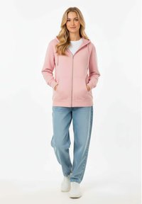 Felpa rosa chiaro con zip e tasca frontale, indossata su una maglietta bianca. Jeans blu a vestibilità ampia e sneakers bianche completano l'outfit.