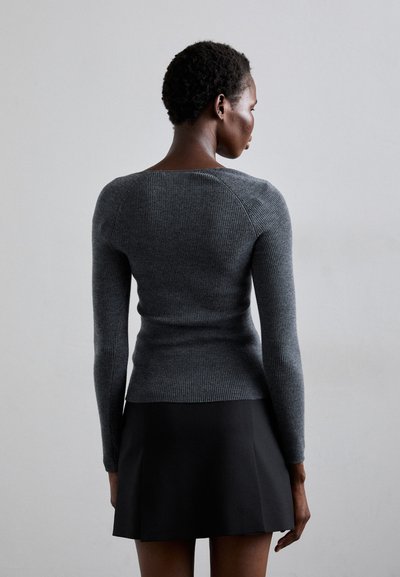 Grey ribbed long-sleeve sweater with a round neckline, fitted silhouette, and textured fabric, paired with a black flared skirt.