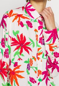 Košile s dlouhým rukávem a límečkem z lehké látky s výrazným květinovým vzorem v červené, růžové, oranžové a zelené na bílém pozadí.