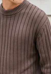 Pull en tricot côtelé marron avec un col haut texturé et des rayures verticales. Le tissu a une apparence tissée douce et un léger stretch.