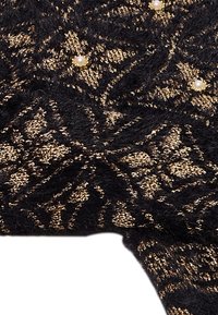 Tela negra con un patrón texturizado en dorado, con pequeños acentos de perlas. Textura suave y esponjosa con detalles intrincados en toda la superficie.