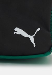 Sac de sport noir avec une finition texturée, présentant un logo de puma blanc en train de sauter et des accents en mesh vert le long des bords.