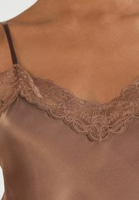 Brun satäng slip camisole med en delikat spetskant längs V-ringningen och tunna, justerbara axelband med en slät textur.
