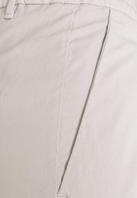 Pantaloni beige in tessuto leggero, con una trama liscia, cuciture visibili e tasche laterali, in un design su misura.