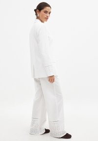 Valge linane bleiser, millel on krae ja lõhud külgedel, koos laia säärega valgete pükstega, mille äärtes on tikandid.