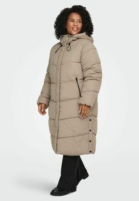 Bēšs pūtēts mētelis ar kapuci, aprīkots ar rāvējslēdzēju priekšpusē, sānu kabatām un sprādzēm apakšmalā. Quilted dizains un mīksta tekstūra.