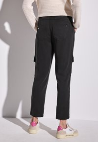 Schwarze Cargo-Hosen mit zwei Gesäßtaschen und seitlichen Cargo-Taschen, kombiniert mit beigen Sneakers mit einem pinken Absatz.